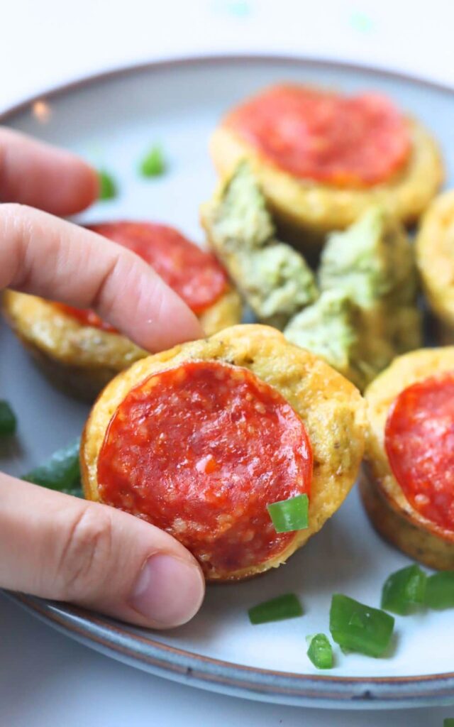 fingers holding a healthy mini pizza muffin with a pepperoni on top