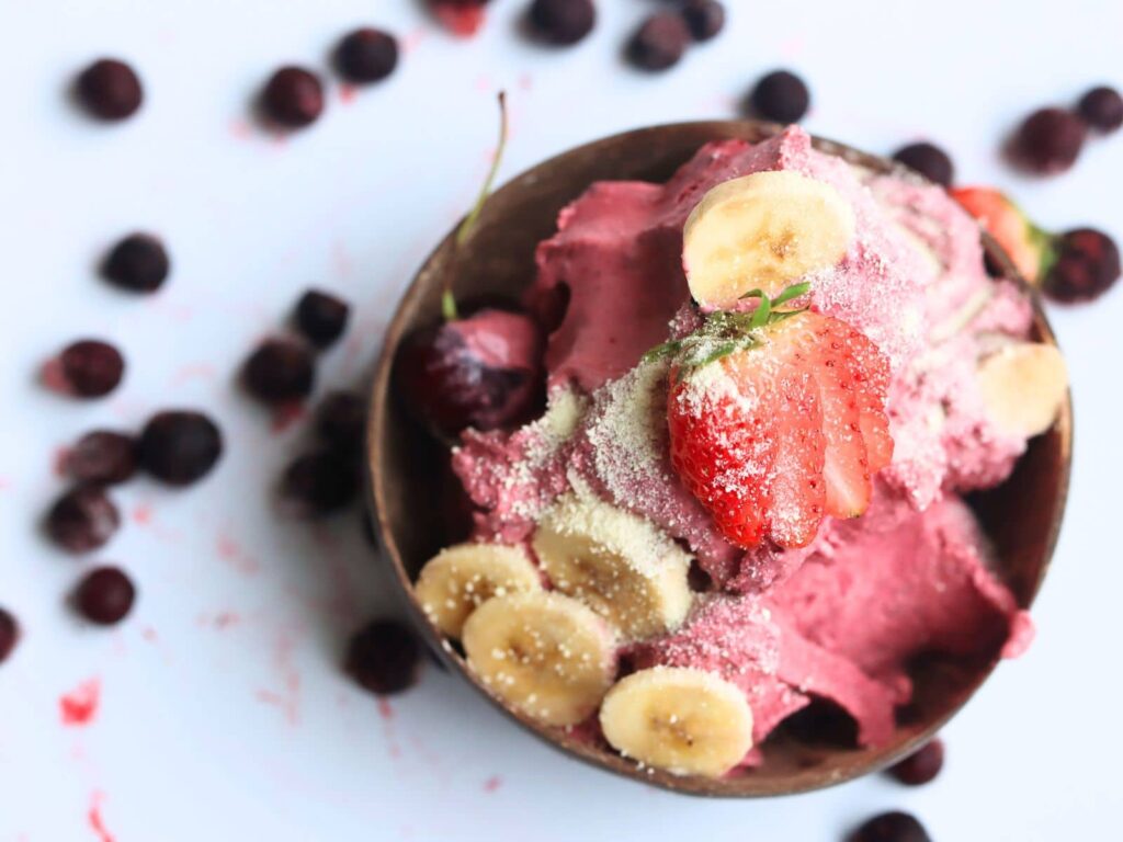 top-down view of acai ice cream in a coconut wood bowl with mixed berries on top