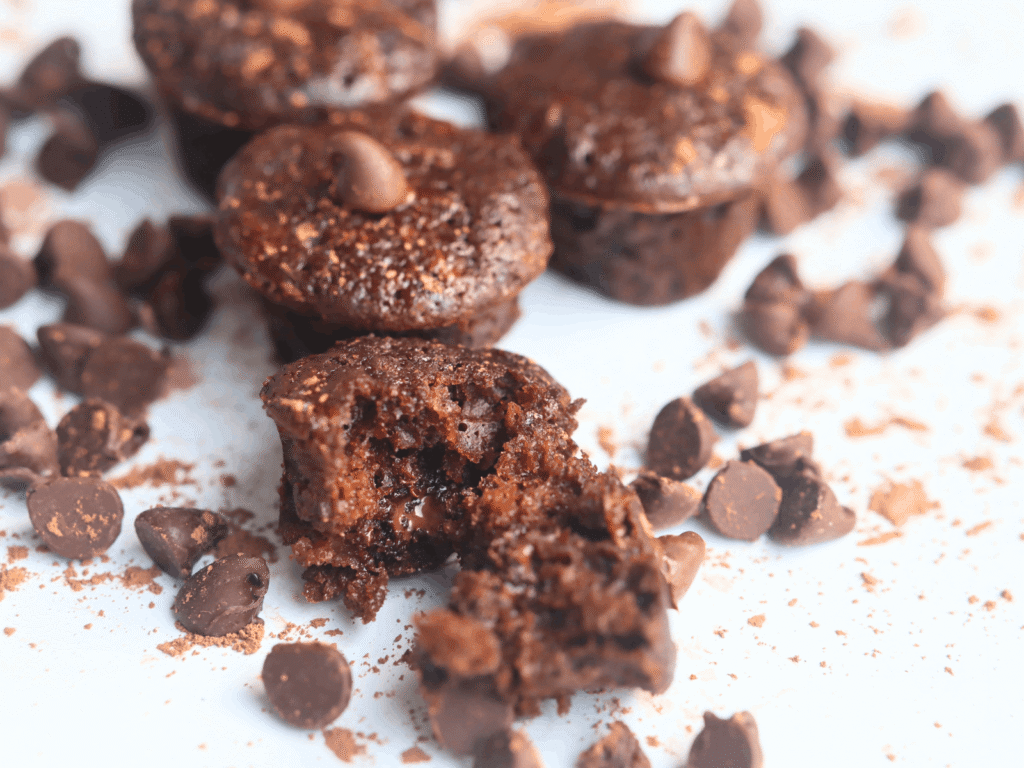 chocolate zucchini mini muffin broken open in front of other muffins and chocolate chips