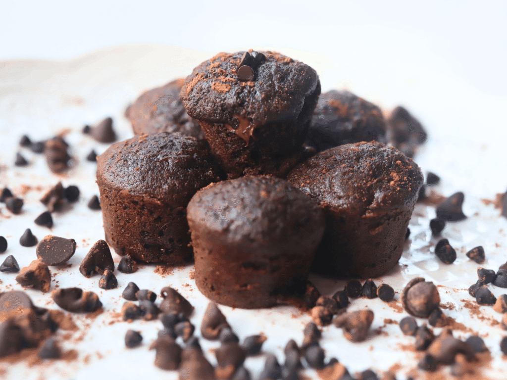 whole wheat double chocolate muffins in a pile on a white plate with chocolate chips