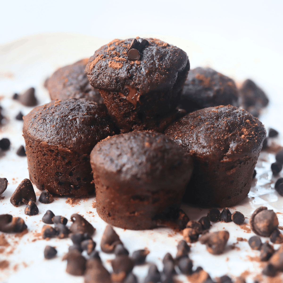 a stack of chocolate mini muffins made with whole wheat flour and zucchini surrounded by chocolate chips