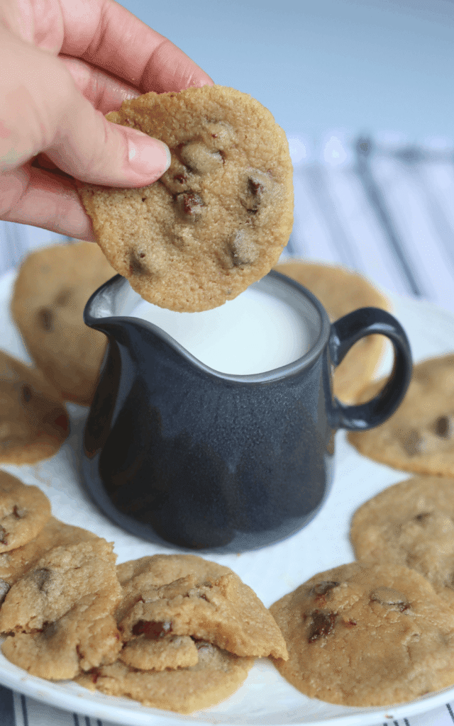 hand dipping a whole wheat chocolate chip cookie made with powdered milk into a pitcher of milk